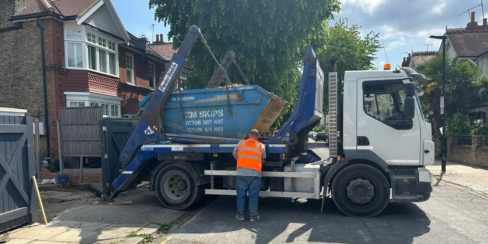 ZM Skips driver delivering a blue skip for domestic waste removal in a residential area of Greenford.